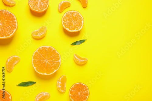 Flat lay composition with halves of fresh ripe tangerines and leaves on yellow background, space for text. Citrus fruit