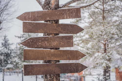 Wooden direction sign with snow on it and with snowfall on background