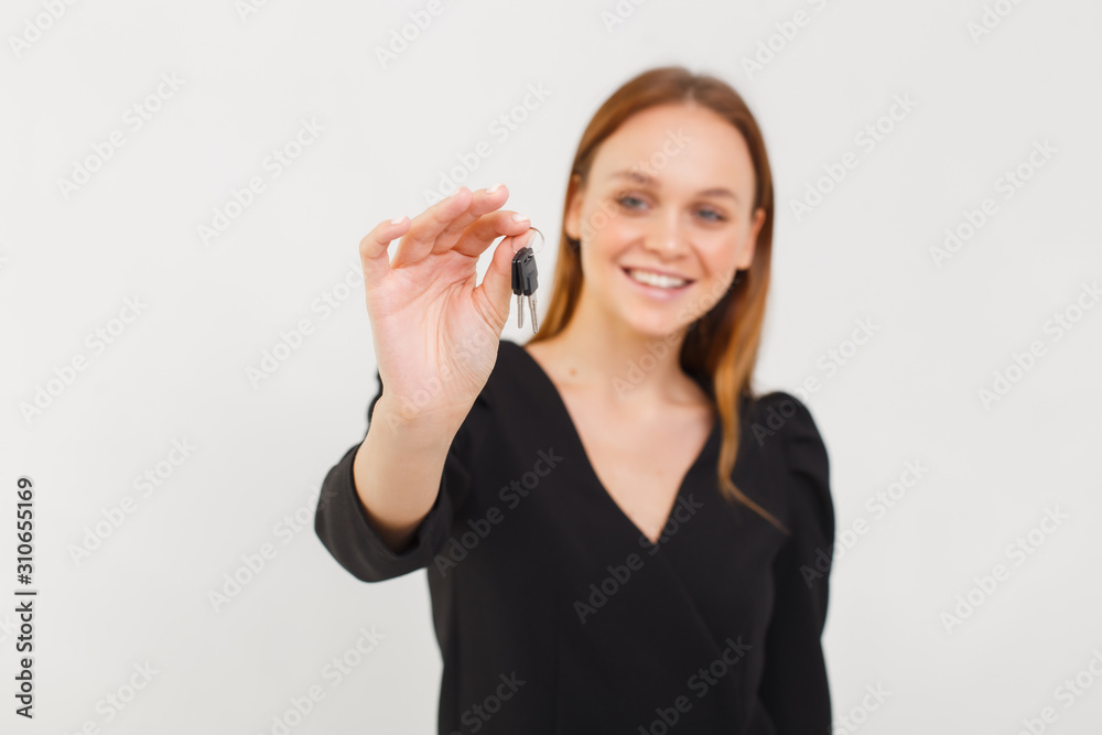 young woman holding out keys towards camera on white seamless background with selective focus