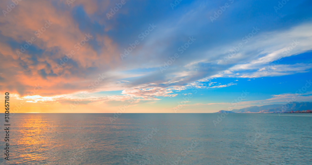 Sunset over the sea and mountains, cloudy sky 