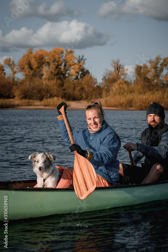 Happy couple with dog in canoe at sunset.