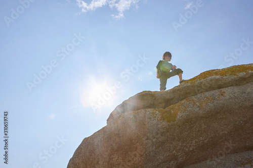 Proud boy standing on a big rock and smiling, blue sky, sun flares © stock mp