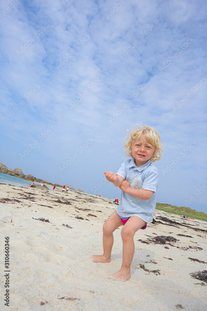 Suspiciously looking cute little boy in the sand of a beach, summer holiday