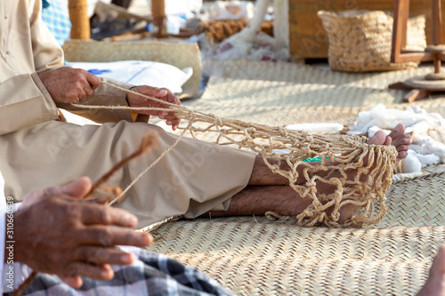 Old man is knitting traditional fishing net, hands in frame