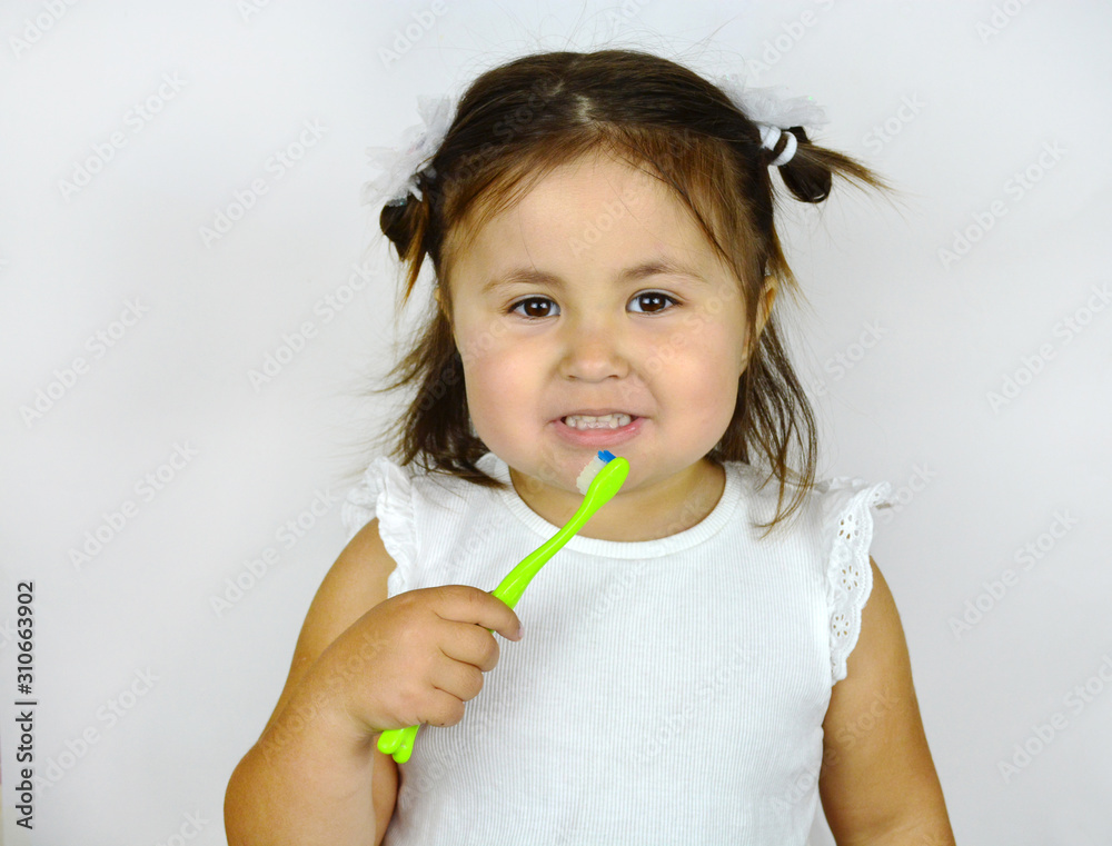 Close-up portrait of a beautiful toddler smiling while brushing her teeth. Little girl brushing teeth with toothbrush over white background with copy space. Dental healthcare and oral hygiene concept Close-up portrait of a beautiful toddler smiling while brushing her teeth. Little girl brushing teeth with toothbrush over white background with copy space. Dental healthcare and oral hygiene concept