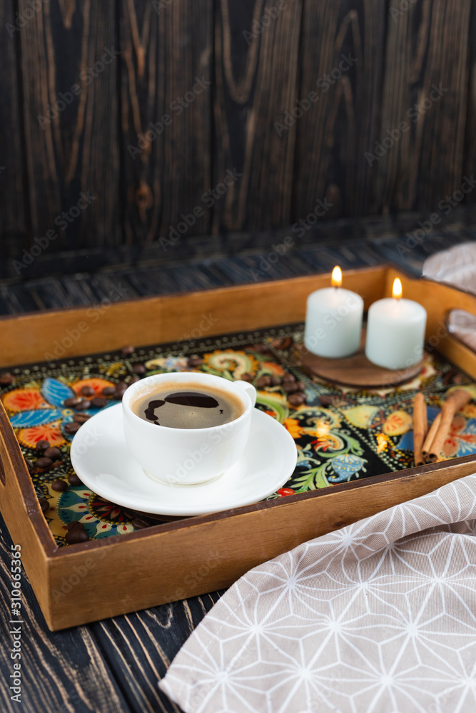 A white cup of coffe staying on a fancy tray with traditional decorative painting style - Ukrainian Petrykivka - on dark wooden background