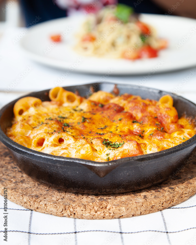 Baked macaroni and cheese with fresh tomato sauce served on hot pan Baked macaroni and cheese with fresh tomato sauce served on hot pan