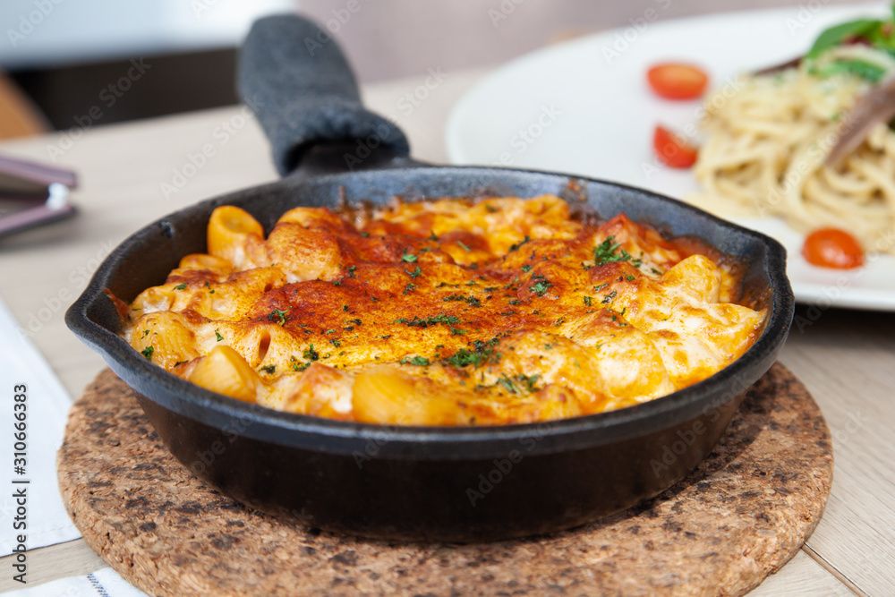 Baked macaroni and cheese with fresh tomato sauce served on hot pan Baked macaroni and cheese with fresh tomato sauce served on hot pan