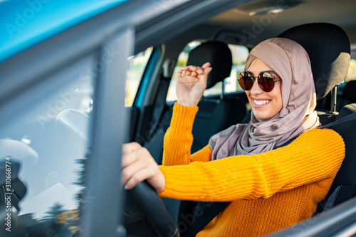 Beautiful  Muslim woman driving a car wearing hijab. Emirati woman driving a car in Dubai at sunset. Portrait of a Middle Eastern woman driving a car, she is wearing a modern beige Abaya. photo