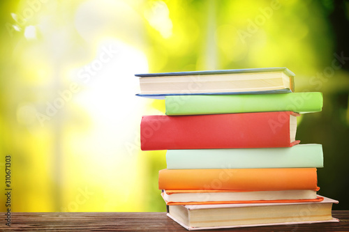 Stack of colorful books on wooden table against blurred green background. Space for text