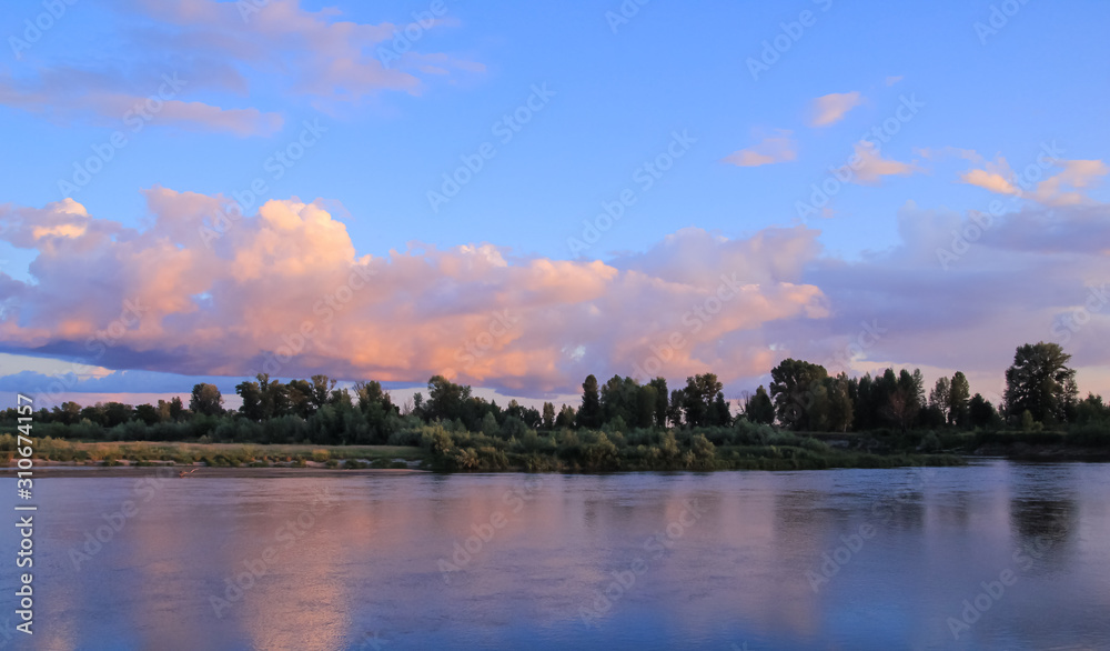 Naklejka premium Sunset on the river with the bank covered by small forest and blue-pink sky