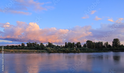 Sunset on the river with the bank covered by small forest and blue-pink sky