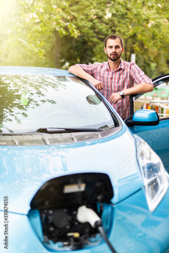 Handsome man plugging cable to electric car