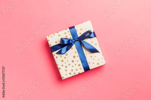 wrapped Christmas or other holiday handmade present in paper with blue ribbon on living coral background. Present box, decoration of gift on colored table, top view with copy space