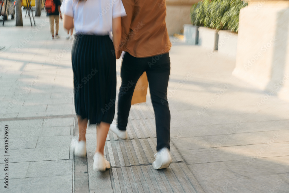 Lower body section of a young tourist couple walking by store windows and holding paper shopping bags in a destination city. Lower body section of a young tourist couple walking by store windows and holding paper shopping bags in a destination city.
