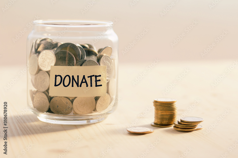 Coins in glass jar with DONATE word written text label for giving and donation concept Coins in glass jar with DONATE word written text label for giving and donation concept