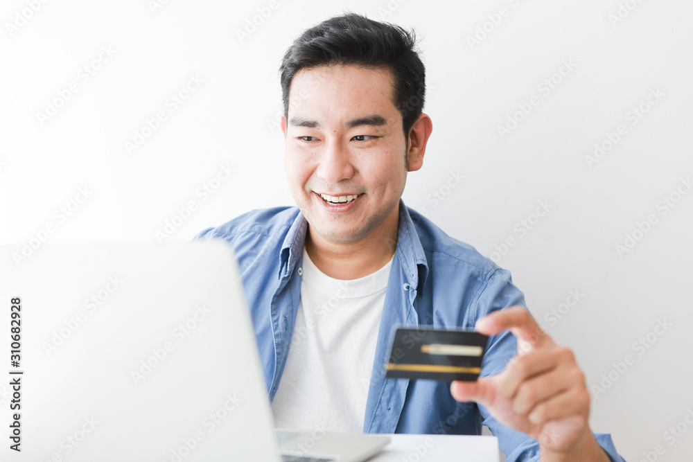 Asian handsome man in blue shirt using credit card with laptop computer shopping online Asian handsome man in blue shirt using credit card with laptop computer shopping online