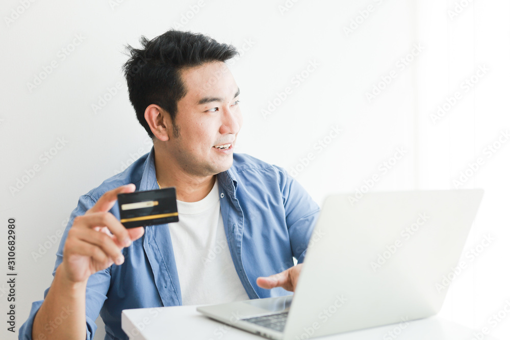 Asian handsome man in blue shirt using credit card with laptop computer shopping online Asian handsome man in blue shirt using credit card with laptop computer shopping online