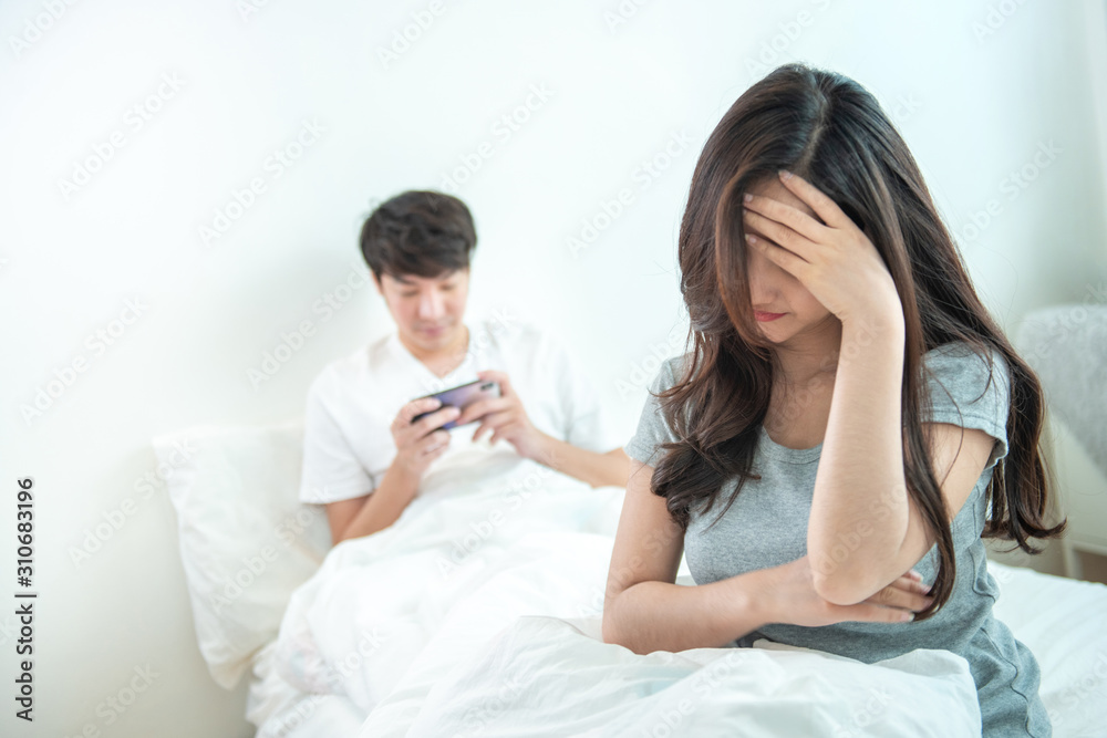 Young asian woman is upset that man uses phone all the time without paying attention to her. Man holds phone pay attention on smart mobile phone while sit on bed with ignoring on his girlfriend. Young asian woman is upset that man uses phone all the time without paying attention to her. Man holds phone pay attention on smart mobile phone while sit on bed with ignoring on his girlfriend.