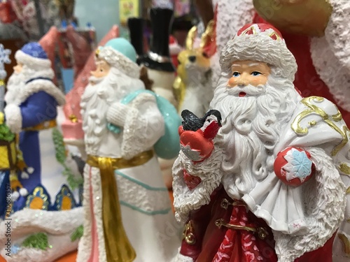 Toy Santa Claus in a red suit with a bullfinch in his hand on the background of other Santas in the store. Photo with mobile under shop lighting.