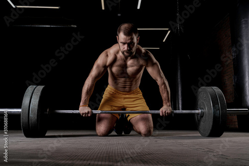 Strong weightlifter with muscular body prepares to lift the barbell