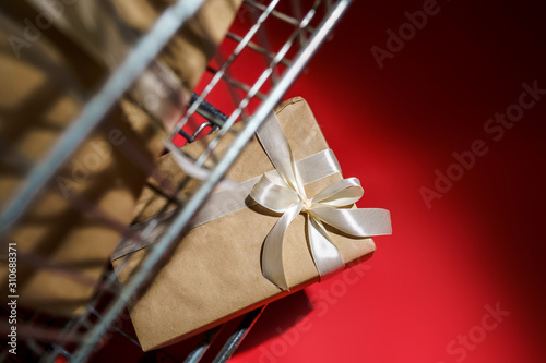 Supermarket basket with gifts wrapped in craft paper with a white ribbon on a red background