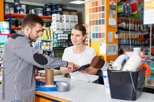 Young female seller standing at the counter in household tools store