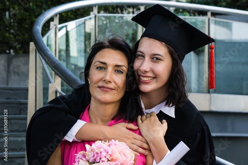 Young beautiful woman graduate hugging her mother at graduation ceremony, University Graduation Certificate Hugging Success Family Concept.