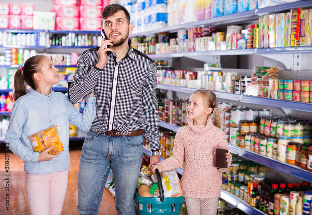 Man speaking phone during shopping with two little girls in grocery store