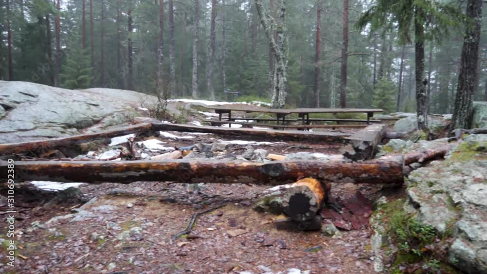 Picnic tables and logs lashed together to form sitting benches around a fire pit at a clearing in the forest on a damp and misty day Picnic tables and logs lashed together to form sitting benches around a fire pit at a clearing in the forest on a damp and misty day