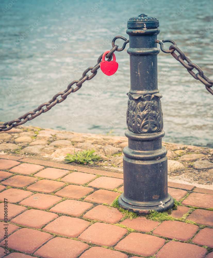 Railing Post on Pier with a padlock in the shape of heart hanging on a chain A Railing Post on Pier with a padlock in the shape of heart hanging on a chain A