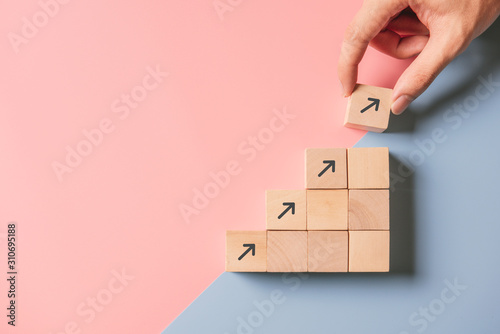 Business concept growth success process, Close up man hand arranging wood block stacking as step stair on paper blue and pink background, copy space. photo