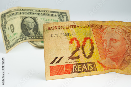 Close up of a bill of 20 Brazilian reals and one US dollar bill located behind, isolated on white background