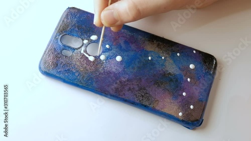 Hand of a teenager draws a zodiac sign on a background of the starry sky. DIY. Handmade mobile phone case.