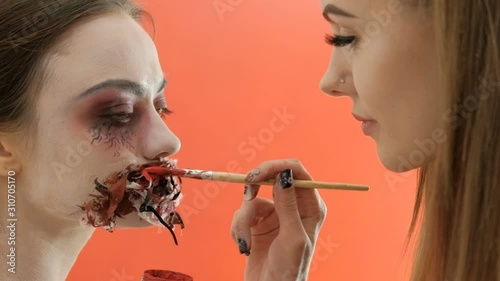 Girls are preparing for a meeting of Halloween. Festive makeup for All Saints Day. Horror party or carnival. Sewn mouth and bloody paint on a brush in the female hand of a beautiful young woman.