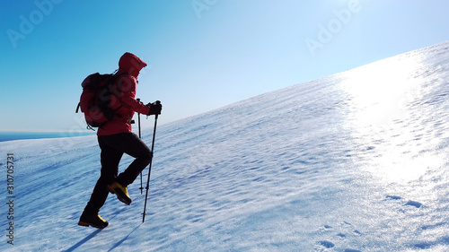 Mountaineer climbs a snowy mountain over blue clear sky. Winter