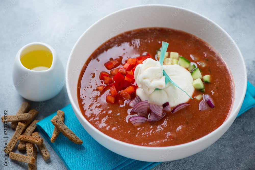 Tomato gazpacho with burrata cheese, chopped bell pepper, red onion, cucumber and olive oil served in a white bowl Tomato gazpacho with burrata cheese, chopped bell pepper, red onion, cucumber and olive oil served in a white bowl