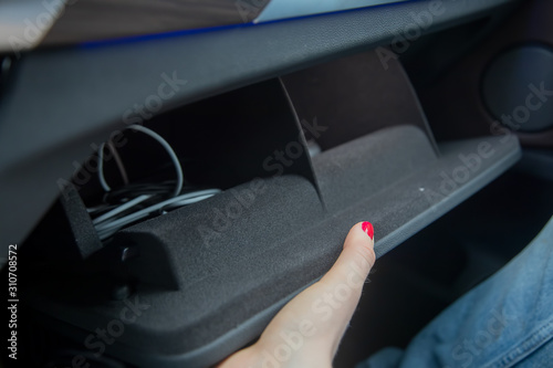 female hand opens a glove box in a black car interior. there are cables inside. close-up, soft focus.