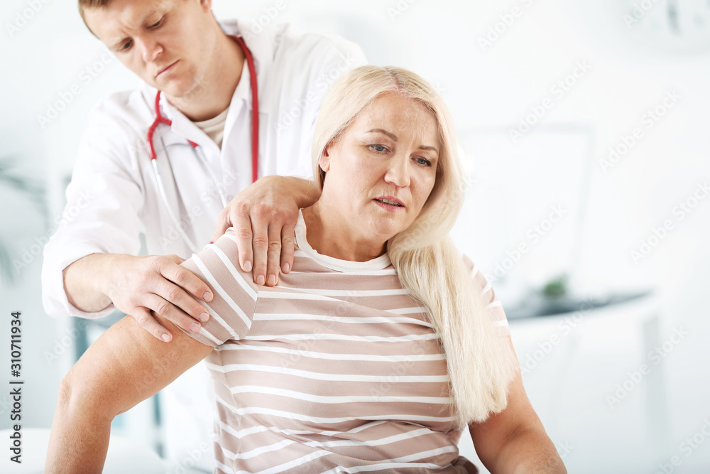 Doctor examining mature woman with joint pain in clinic Doctor examining mature woman with joint pain in clinic