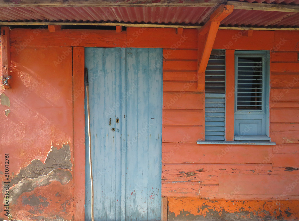 Rusted blue front door and window over orange facade. Tropical construction. Martinique, Antilles. French West Indies Rusted blue front door and window over orange facade. Tropical construction. Martinique, Antilles. French West Indies