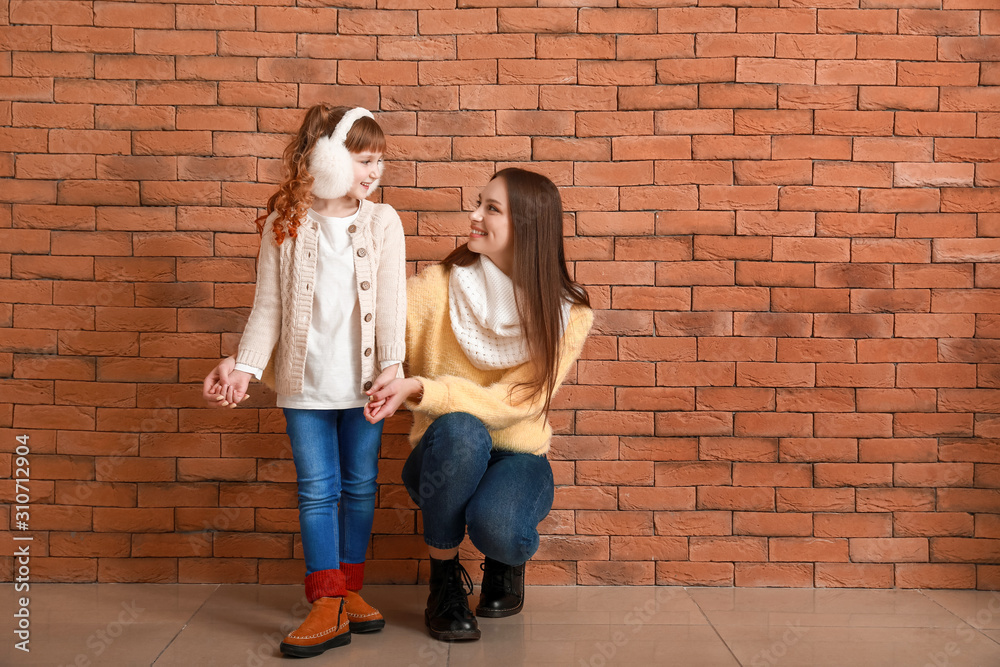 Cute little girl with mother in winter clothes near brick wall