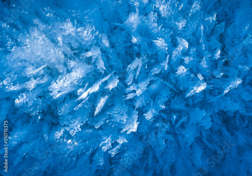 blue texture of an ice surface with pure azure water ,cold snow cryslallized wall background ,winter frozen lake side close up , abstract macro wallpaper
