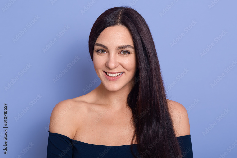 Fototapeta premium Image of young beautiful gorgeous young woman with perfect skin wearing dark blue dress posing with bare shoulders. Beauty fasion and care concept, attractive girl looks smiling directly at camera.
