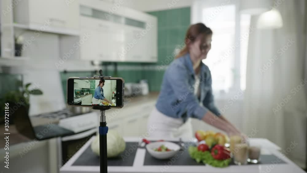 modern housewife blogger records video content on smartphone for his vlog, talks about proper nutrition shows a diet plan looks in camera and thumbs up standing at table with with fresh vegetables modern housewife blogger records video content on smartphone for his vlog, talks about proper nutrition shows a diet plan looks in camera and thumbs up standing at table with with fresh vegetables