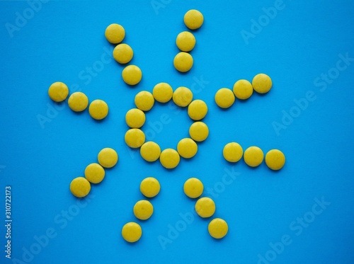 Yellow shape of sun made of candy, on blue solid background with copy space.