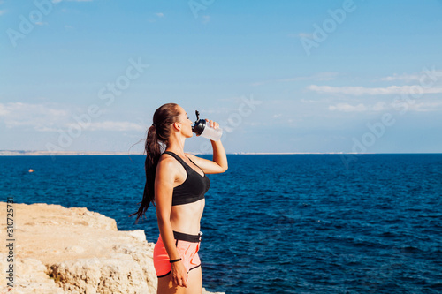 Fitness girl drinking water from a shaker after a workout on the beach