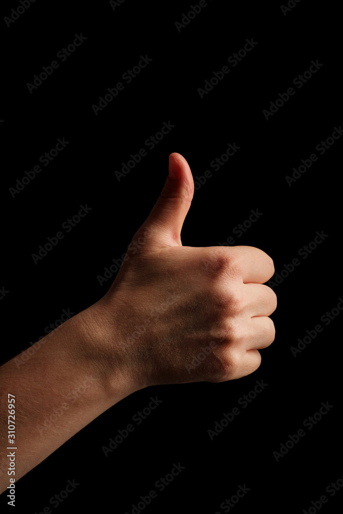 A young woman hand is displaying a thumbs up, indicating that he likes or approves of something. Female hand on a black background shows like. Copy space. A young woman hand is displaying a thumbs up, indicating that he likes or approves of something. Female hand on a black background shows like. Copy space.