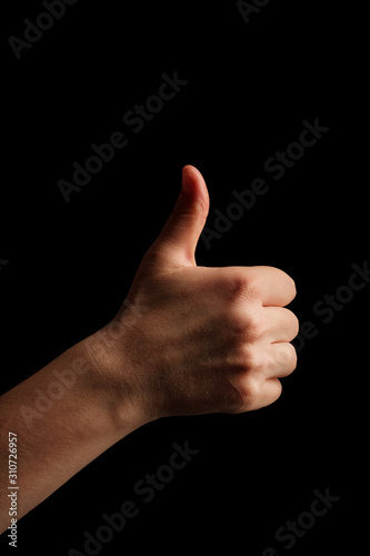 A young woman hand is displaying a thumbs up, indicating that he likes or approves of something. Female hand on a black background shows like. Copy space.