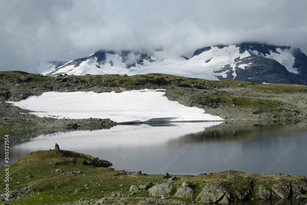 Beautiful mountain landscape with snow patches on the rocks, impressive grey clouds and a lake on Sognefellsvegen in Summer