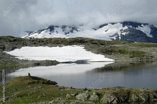Beautiful mountain landscape with snow patches on the rocks, impressive grey clouds and a lake on Sognefellsvegen in Summer